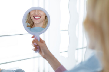 Female patient looking at her beautiful healthy white smile in dental mirror reflection,...