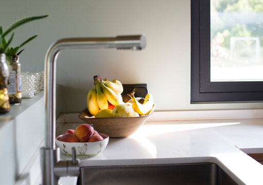 Frutera de madera con bananas, otra de ceramica con duraznos apoyadas en la mesada de una cocina