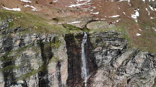 Aerial drone view of the mountain shelter Bivacco Piano della Parete in Switzerland. Surrounded by mountains and a waterfall, silence and serenity prevail. Outdoor adventure and a traveling lifestyle.