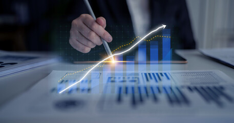 A business professional analyzes financial trends, using digital graphs and charts in a modern...