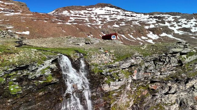 Aerial drone view of Bivacco Piano della Parete in Switzerland. A couple enjoying a peaceful mountain view, surrounded by mountains and a waterfall. Outdoor adventure lifestyle. 