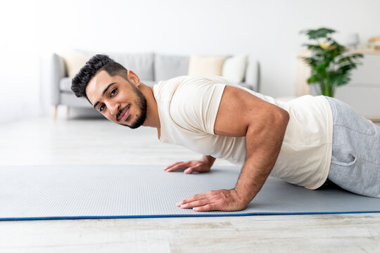 Millennial Arab man standing in plank pose on yoga mat, doing strength exercises at home. Fit Eastern guy doing push ups, leading active lifestyle during coronavirus quarantine