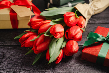 Red tulip bouquet with gift boxes. Easter or birthday holiday black background.