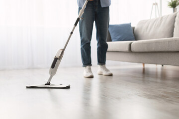 Closeup cropped low section of woman washing hardwood laminate flooring using water spray mop pad and refillable bottle with cleaning agent. Chores Concept. Blurred Background, Free Copy Space