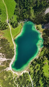 Vertical aerial drone view of the Alps and the green Seebensee on a sunny summer day. A couple enjoys the view of Seebensee and goes hiking. Seebenlake	
