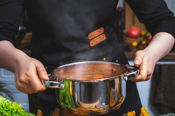 Housewife holding stainless pot with steaming dish in home kitchen during autumn meal preparation with fresh vegetables for healthy cooking visuals. Home lifestyle, healthy meals, cooking content.