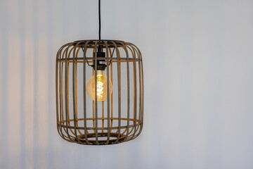 Close-up of rustic pendant light with exposed bulb inside open rattan-style cage design