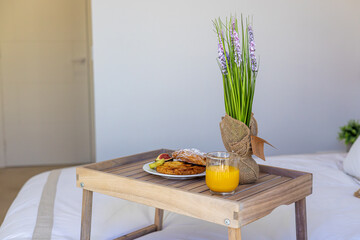 Breakfast in bed on wooden tray with juice, pastry and lavender plant in cozy bedroom