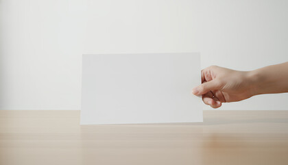Hand Holding Blank White Paper Card Mockup on Wooden Desk. Horizontal Document or Flyer Template Presentation.
