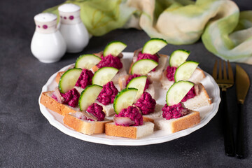 Canape with salted herring, beetroot mousse and cucumber on white bread toasts