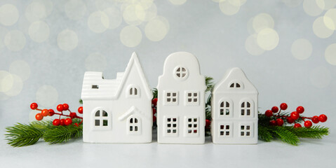Three white ceramic houses with pine branches and red berries, soft bokeh background, winter...