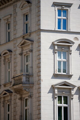 Obraz premium Historic building facade with tall windows, decorative frames and balcony, strong daylight casting sharp shadows, highlighting classical urban architecture, texture, symmetry, and timeless city charac
