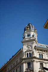 Obraz premium Historic clock tower with ornate facade and domed roof rising against clear blue sky, detailed classical architecture emphasizing time symbolism, urban heritage, and timeless city landmark presence.
