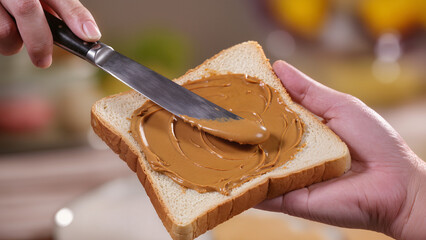 Hands spreading creamy peanut butter on white bread with knife.