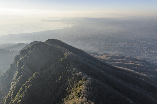 Aerial view of rugged mountain peaks, draped in shadows, meet the misty horizon in a blend of earthy tones and ethereal light, Ercolano, Campania, Italy.
