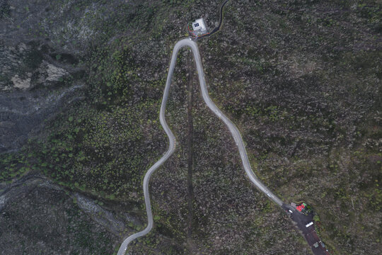 Aerial view of a winding road slicing through the rough, dark terrain towards a solitary building on Sentiero del Gran Cono, Ercolano, Campania, Italy.