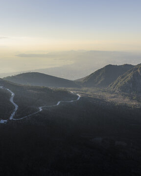 Aerial view of the winding Sentiero del Gran Cono cutting through the dark, rugged landscape of Vesuvius National Park under a soft, hazy sky., Ercolano, Campania, Italy.