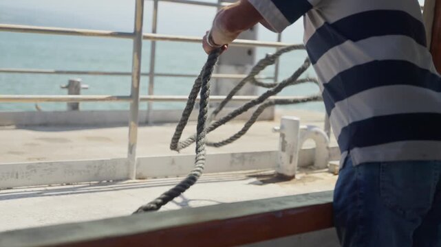 Crew member throwing rope from boat is before docking in marina or port. Small wooden tour boat in Holy Land Israel is nearing pier as sailer uses rope to tie it in Sea of Galilee religious visit