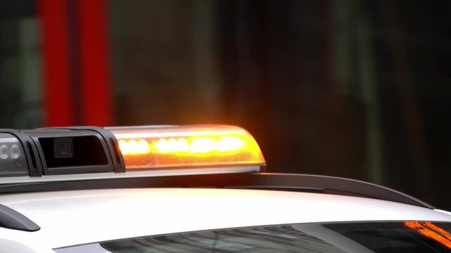 Close-up of flashing amber emergency light bar on white service vehicle roof. Orange warning lights glowing for road assistance or security. Safety and traffic control concept.
