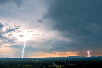 Lightning flashes across dark sky while storm clouds gather over distant mountains during twilight.