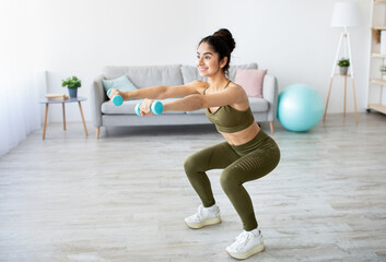 Strength workout concept. Fit Indian woman doing squats with dumbbells at home, free space....