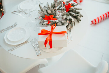 Elegant table setting with white plates, silverware, and a festive gift wrapped with a bright red...