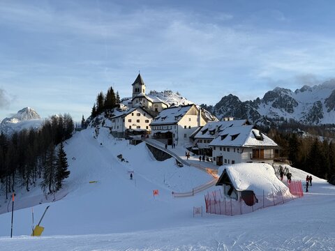 Scenic view Monte Lussari alpine village snowy mountains; ski resort winter vacation Alps landscape. Tarvisio Italy ski slope church mountain peaks tourism destination. Travel destination winter sport