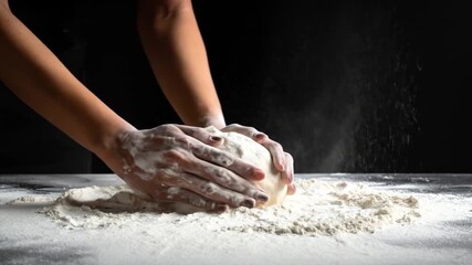 Hands kneading dough covered in flour with more flour falling in a dark kitchen