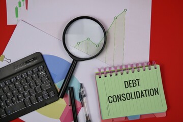 A desk setup featuring a green notebook labeled debt consolidation, a magnifier, charts, and a keyboard, illustrating financial analysis, budgeting, and planning for debt reduction and financial goals