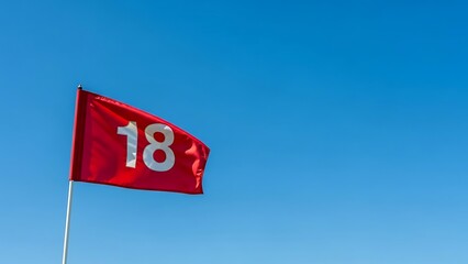 A red golf flag with the number 18 on it, waving in the wind against a clear blue sky.