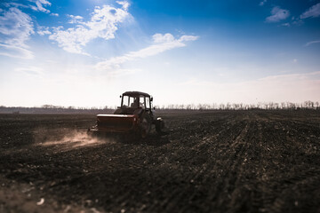 Blue tractor pulling a seed drill machine during spring sowing season. Agricultural landscape with a tractor.