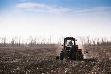 Blue tractor pulling a seed drill machine during spring sowing season. Agricultural landscape with a tractor.