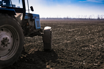 Blue tractor pulling a seed drill machine during spring sowing season. Agricultural landscape with a tractor.