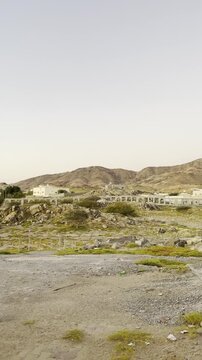 A desert view near Madinah with rocky terrain, distant historic buildings, surrounding mountains, featuring the Maqbarat Shuhada Badr sign and the solemn landscape of a historic pilgrimage site.