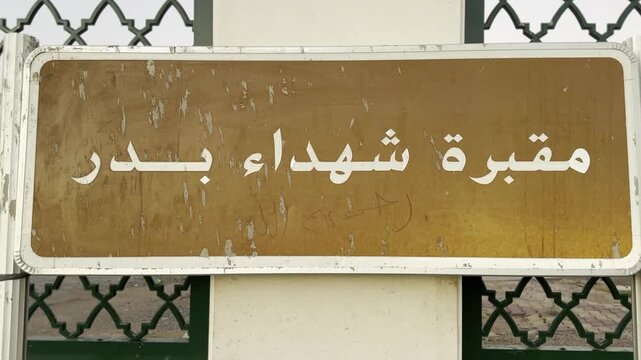 A weathered sign marking the Cemetery of the Martyrs of Badr, a solemn historic site linked to early Islamic battles, remembrance, and pilgrimage heritage in the region.