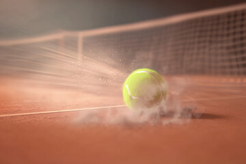 Tennis ball striking a clay court with motion blur and dust particles near a net.