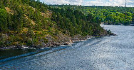 Rocky forested coastline along calm blue water.