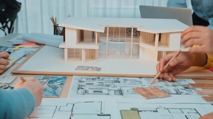 A dynamic scene of professionals collaborating on an architectural project. A detailed model and blueprints are spread across the table in a modern office setting. SACTR - Powered by Adobe