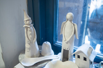 Handcrafted white clay figurines of an angel and a stylized figure displayed in a shop window in Nazareth.