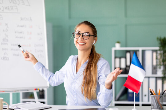 A joyful young professor teaches a French class online, pointing at the blackboard that displays essential grammar rules. She actively engages students with her explanations about tenses.
