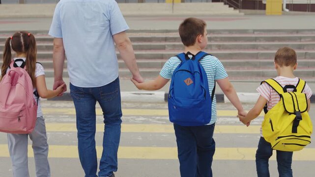 Father walking children to school, Safe crossing at crosswalk, Kids with backpacks, Back to school morning, Family on zebra crossing, Parent protecting kids, School building in background, Siblings