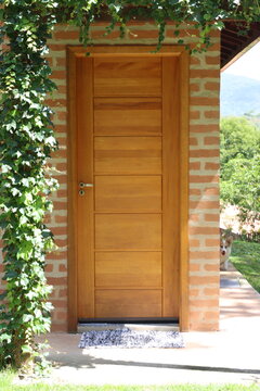 A modern wooden door is framed by lush green ivy and a brick wall, with a playful dog visible in the background