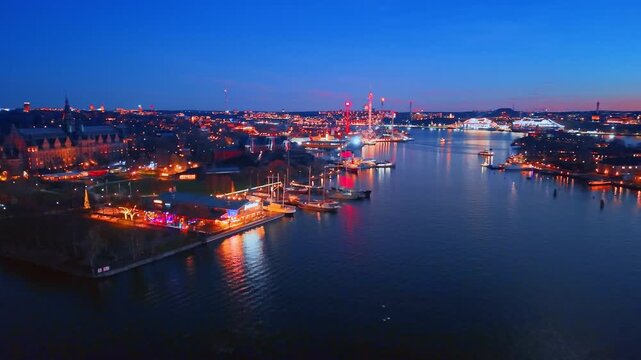 Moving over the dark peaceful waterscape of the lake in Stockholm, Sweden. View on stunning luminous cityscape at night.