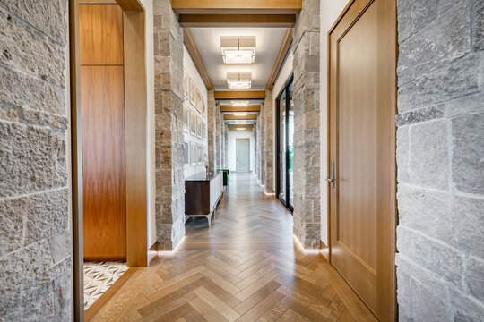 modern luxurious interior hallway stone walls rough hewn rustic herringbone flooring modern lighting wood accents cabinet architectural design rock pillars long depth high end residential foyer entry