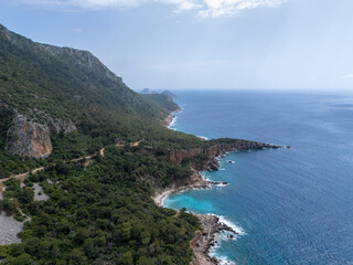 Fototapeta premium Aerial view of Adrasan, with its calm turquoise waters, a long sandy-pebble beach, and forested mountains in Antalya, Turkey.