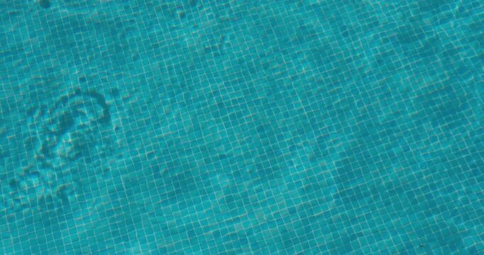 PORTOCOLOM, MALLORCA, SPAIN - OCTOBER, 2025: The close-up reveals the soft ripples of water in a swimming pool, sunlight creates patterns on the pool floor, wide shot, summer background.