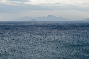 Characteristic features of a Greek island include dry terrain, strong sunlight, blue sea, rocky coastline, and Mediterranean vegetation.