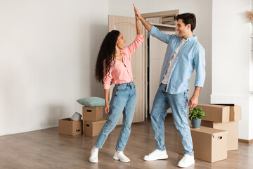 Young couple shares a joyful high five in their new house, celebrating moving day with excitement....
