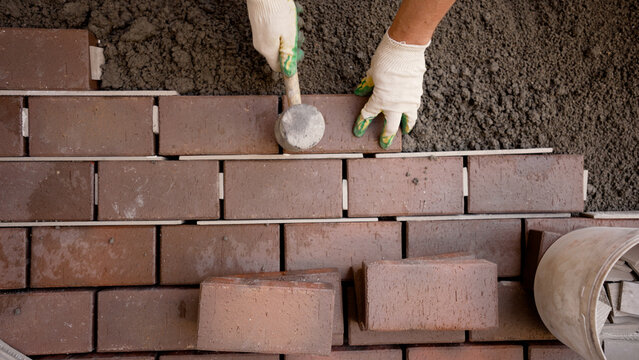 Worker hands laying interlocking pavement bricks with rubber mallet