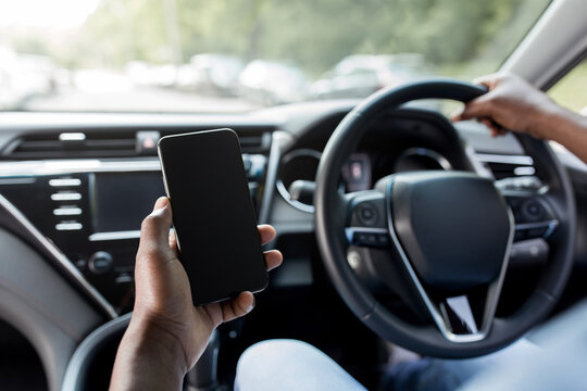Cropped of black man driver holding smartphone with blank screen, mockup. Closeup of mobile phone with empty display in african american guy hand, using mobile app for navigation, copy space